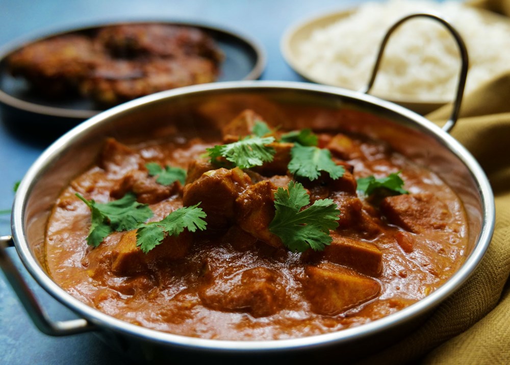 Tofu Tikka Masala in a balti dish served with white basmati rice and onion bhajis and topped with fresh coriander