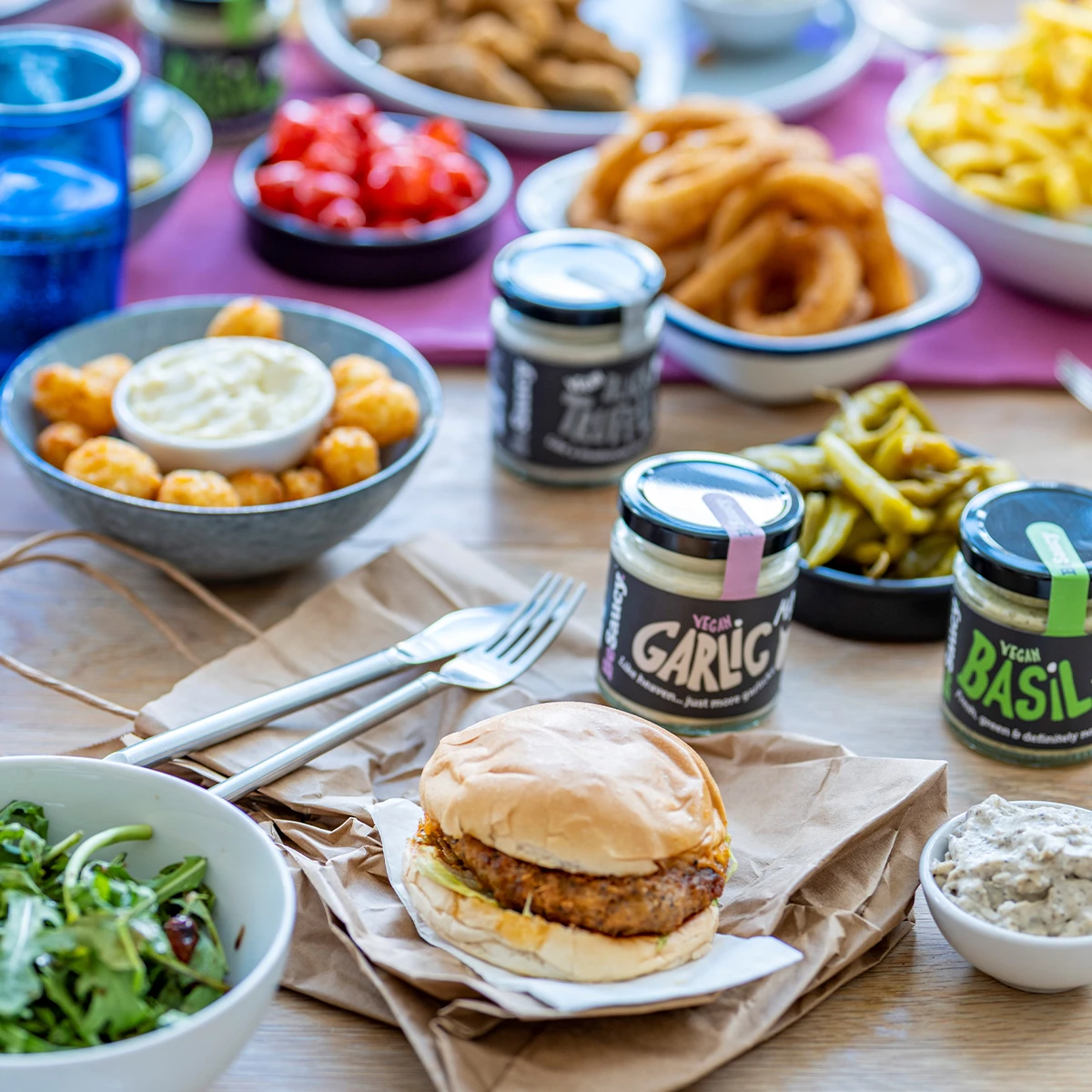 BeSaucy condiments on a table with burgers, salads and other dishes
