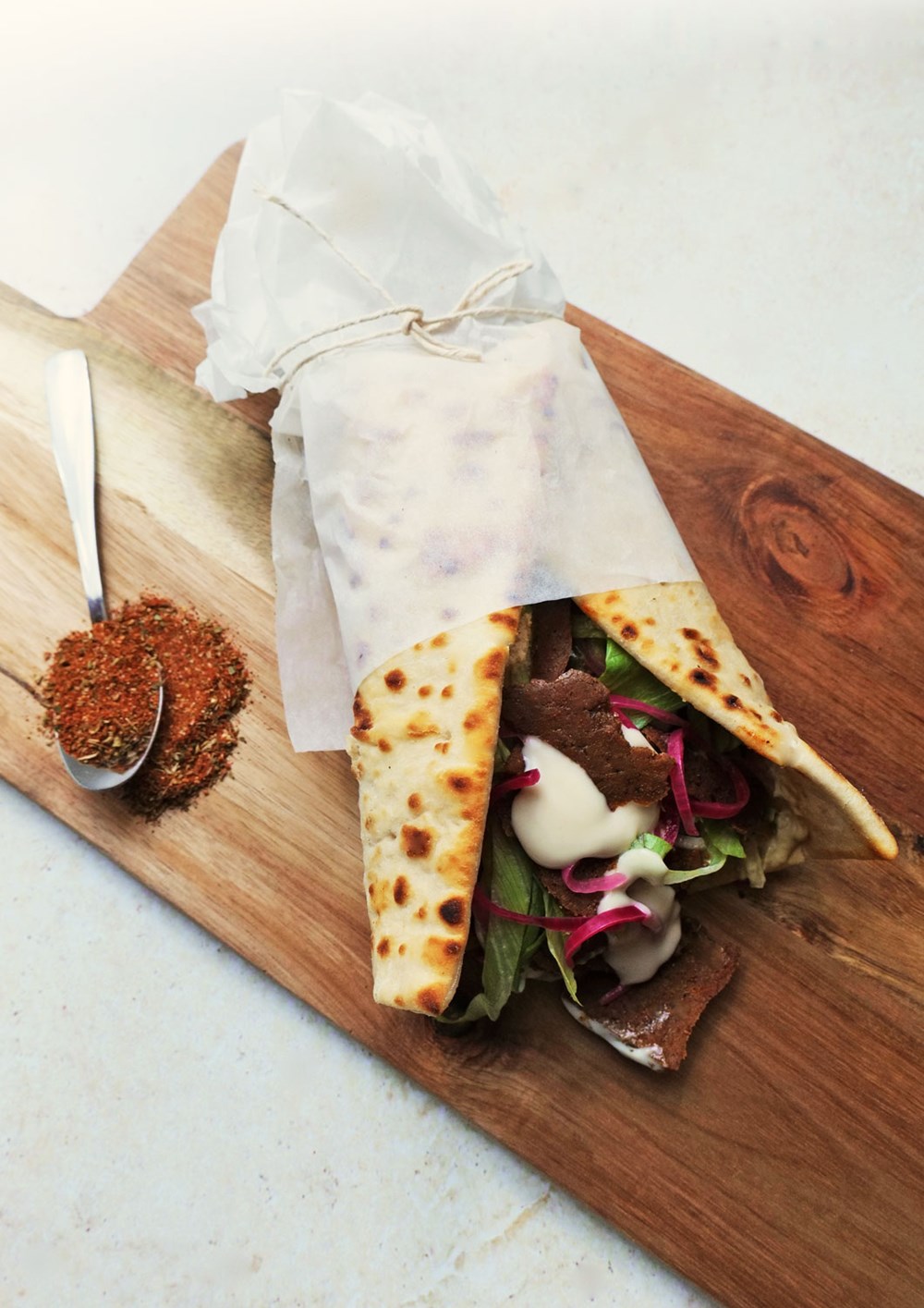 vegan gyros wrap on a wooden serving platter with a spoonful of gyros spice mix